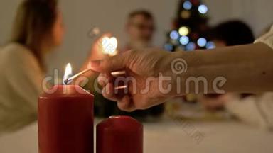 妇女点燃餐桌上的蜡烛，用于圣诞节或新年晚餐。 餐桌和大家庭背景